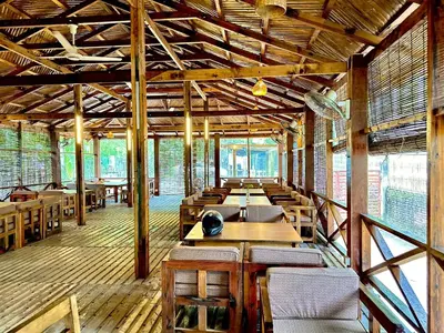 a restaurant with wooden tables and chairs and windows at Bruce House in Nonthaburi
