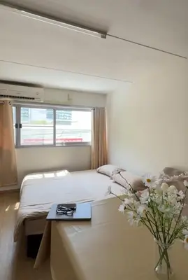 a white bedroom with a bed and a vase of flowers at Happy Daisy ห้องพัก เมืองทองธานี in Nonthaburi