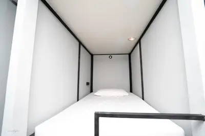 a small white bed in a room with windows at The LODGE BKK Hostel in Bangkok