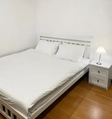 a bed with white sheets and a night stand with a lamp at Apartment studio at platinum in Bangkok