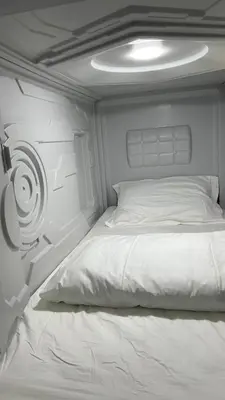 a white bed in a small room with a wall at Kiwi Capsule Hotel in Bangkok