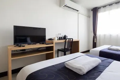 a room with two beds and a desk with a television at Nature Boutique Hotel Ratchayothin in Bangkok