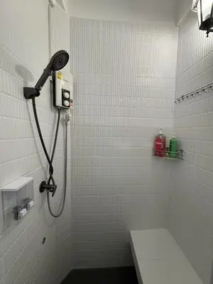 a shower in a white tiled bathroom at The Moment Hostel in Bangkok