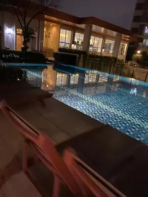 a swimming pool at night with a chair and an umbrella at Appartement douillet pool fitness in Bangkok