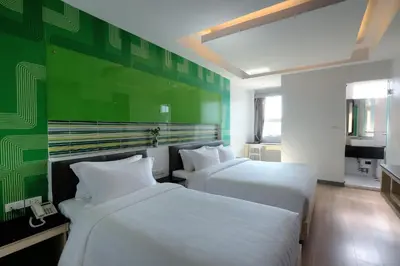 two beds in a room with a green wall at Klassique Sukhumvit Hotel in Bangkok