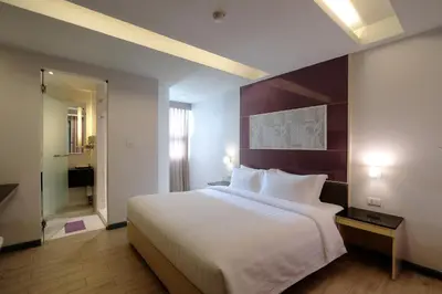 a bedroom with a large white bed and a bathroom at Klassique Sukhumvit Hotel in Bangkok