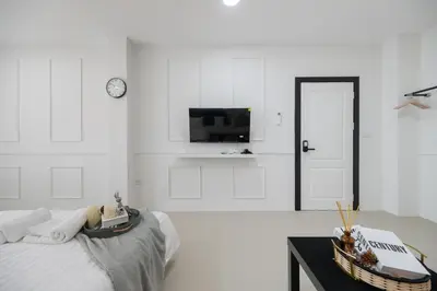 a white bedroom with a bed and a tv at Arun Sa wad - Chinatown in Bangkok