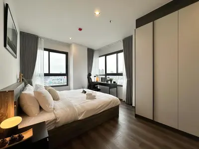 a bedroom with a large bed with a desk and windows at Expansive Stylish 2BR - Ultra Fast Wifi - Asoke in Bangkok