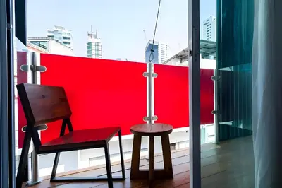 a chair and stool on a balcony with a red wall at XX GO INN Sukhumvit Soi 20 - โกอิน สุขุมวิท 20 BTS อโศก in Bang Kapi