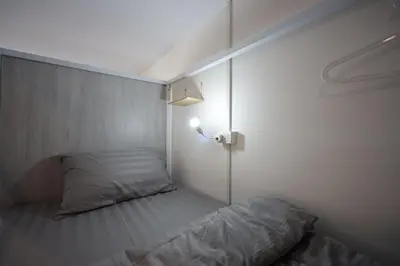 a small room with a bed and a light on the wall at Risa Hostel - Female Only for Solo Travelers in Bangkok