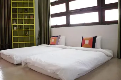 two white beds in a room with a window at The Urbanists BKK Best for groups & long stay near Medpark Hospital , Queen Sirikit Convention hall , Benjakitti Park in Bangkok