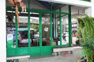 a green store front with a bench in front at The Urbanists BKK Best for groups & long stay near Medpark Hospital , Queen Sirikit Convention hall , Benjakitti Park in Bangkok