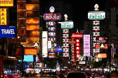 a busy city street at night with many signs at XX GO INN The Grand Palace - MRT Samyot Station in Bangkok