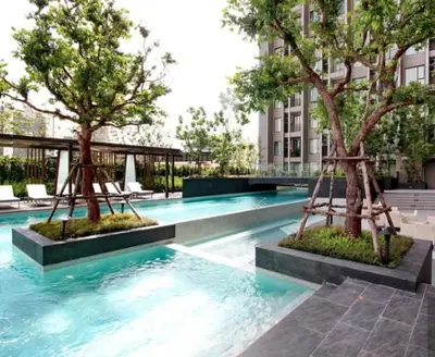 a swimming pool with two trees in front of a building at The Elite Club - ThongLor Bangkok in Bangkok
