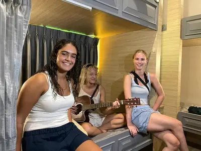 three girls sitting in a bathroom playing a guitar at SU SU khaosan hostels in Bangkok