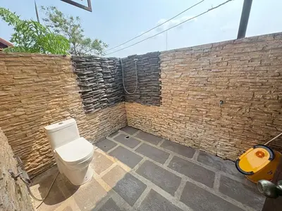 a toilet sitting in front of a brick wall at Baan Marrada Garden in Ban Pak Khlong Khwang