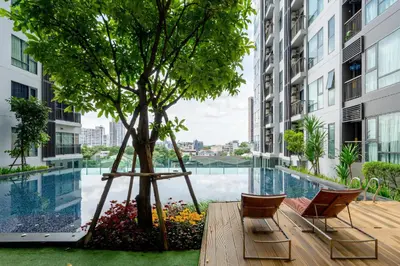 a patio with a tree and chairs and a pool at 5 Star Sukhumvit Condo Infinity Pool Gym Sauna in Bangkok
