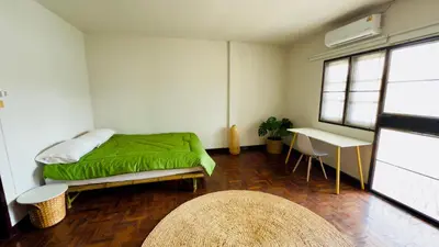 a bedroom with a bed with a green comforter and a table at Creative Bangkok Balcony in Sathani Bang Khen