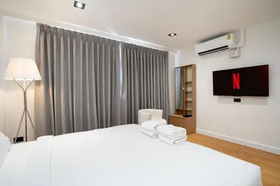 a white bedroom with a large bed and a tv at Townhouse in Khet Phayathai - Ari in Bangkok