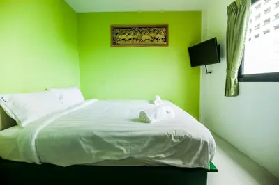 a green bedroom with a bed with white sheets and a television at The Seven Luck in Bangkok