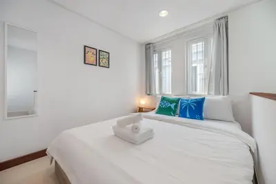 a white bedroom with a large white bed with blue pillows at Moondance House Chinatown in Bangkok