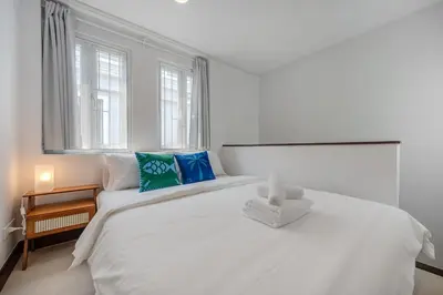 a white bedroom with a large white bed with blue pillows at Moondance House Chinatown in Bangkok