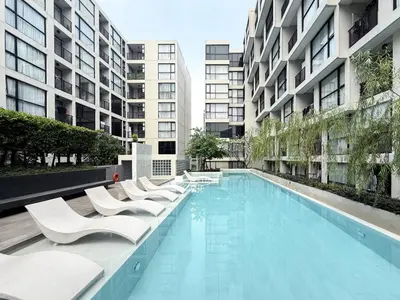 a swimming pool with white chairs and buildings at Serene Tropical 1BR - Ultra Fast Wifi - Sathorn in Bangkok