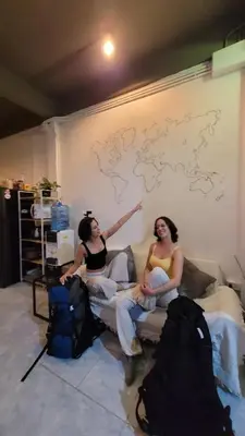 two women sitting on a couch in front of a wall with a map at Casita Hostel House Bangkok in Bangkok