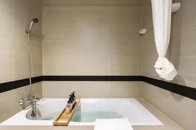 a bathroom with a tub with a shower and a sink at Jungle Dream King Bed Oasis with Balcony & High-Speed WiFi in Khlong Toei
