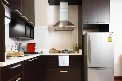 a kitchen with brown cabinets and a refrigerator at King-Suite with Balcony and a full Kitchen near ThonglorBTS in Khlong Toei