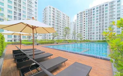 a pool with benches and an umbrella and some buildings at คอนโดศุภาลัยเวลลิงตัน2 in Bangkok