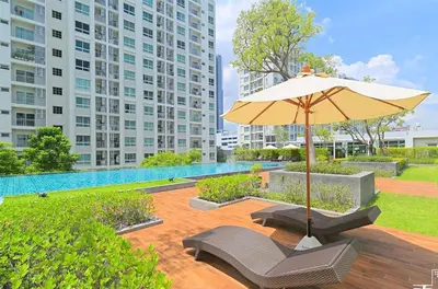 a patio with an umbrella and chairs and a pool at คอนโดศุภาลัยเวลลิงตัน2 in Bangkok