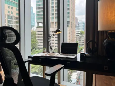 a desk with a laptop and a chair in front of a window at Saladaeng Residences at Silom in Bangkok