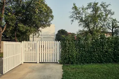 a white picket fence with a hedge and trees at Baan Suanpak in Bangkok