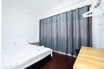 a bedroom with a bed and a table and a curtain at XX GO INN Siriraj Wang Lang - โก อินน์ โรงพยาบาลศิริราช วังหลัง in Bangkok