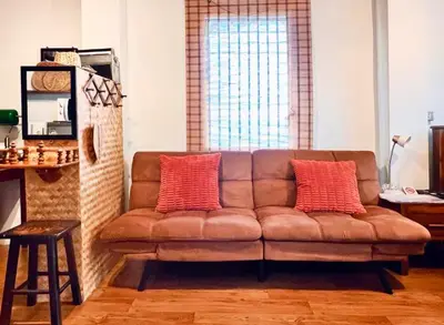 a living room with a brown couch with two red pillows at Baan Ploen Dee - Wat Arun in Bangkok