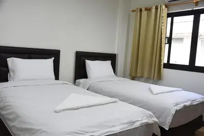 two beds in a room with white sheets and a window at Chaiwat Guesthouse in Bangkok