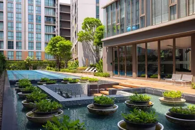 a building with a swimming pool with potted plants at Chambers cher ratchada ramintra in Ban Baen Phichit