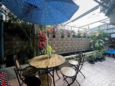 a table and chairs with a blue umbrella in a greenhouse at Baan Alisa 12 in Nonthaburi