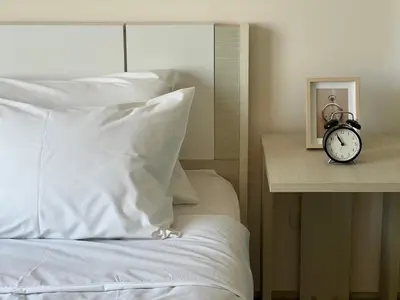 a bed with white sheets and a clock on a table at Cozy8Living in Bangkok 60mto MRT in Ban Bang Khwang