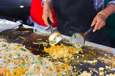 a person cooking food on a grill with spoons at xx GO INN Khaosan Road Bangkok - โก อินน์ ถนนข้าวสาร in Bangkok