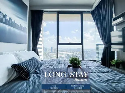 a long stay room with a bed and a large window at Upscale High-Rise 1BR - Ultra Fast Wifi - Phrom Phong in Bangkok