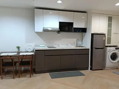 a kitchen with white cabinets and a table and a refrigerator at Modern 59m Sukhumvit 1BR - 31st Floor Pool - Gym in Makkasan