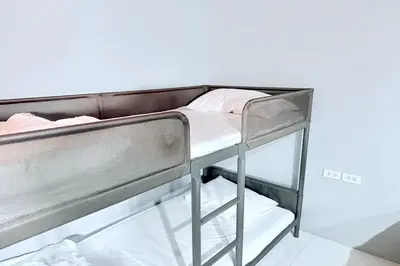a bunk bed with white sheets and pink pillows on it at Sukhum Huai Khwang Guest House in Bangkok