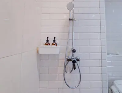a shower in a white tiled bathroom with bottles on a shelf at Panoramic 2BR Ekkamai with infinity pool in Bangkok