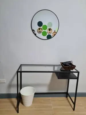 a glass table with a round mirror on the wall at Ananta House in Bang Su