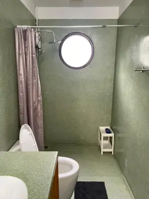 a green bathroom with a toilet and a window at Kin Bangkok in Bangkok