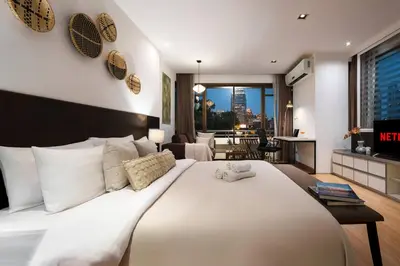 a bedroom with a large white bed and a living room at Quiet Asoke/Nana BTS Retreat w/ Skyline & Gym/Park in Khlong Toei