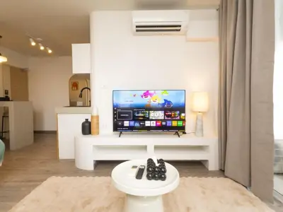 a living room with a large television on a white table at Lovely Studio Room for 2 Guests in the Heart of Sathorn in Bangkok