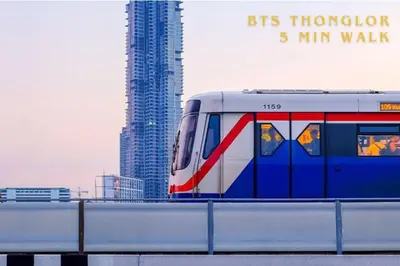 a train traveling on a bridge with a tall building at Chic 1BR |5 min BTS, 2 min to spa|500Mbps&bath-tub in Khlong Toei